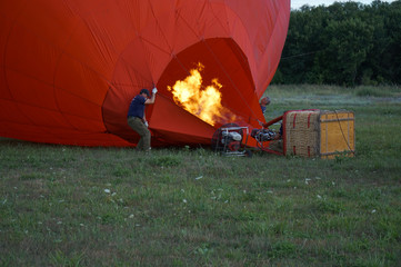 Obraz premium Inflating a balloon lying on the grass with burning air. A fire burning inside the ball 