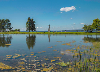 View across lake toward a river with sailboats and  in an urban park and pyramid weathervane