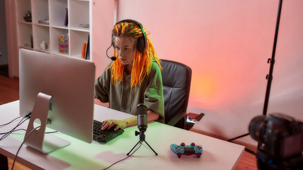 Focus. Female esport gamer, woman in headphones looking focused, playing online video game on PC while recording, filming vlog at home © Svitlana