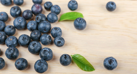 blueberry berries with green leaves on light wooden background top view with copy space