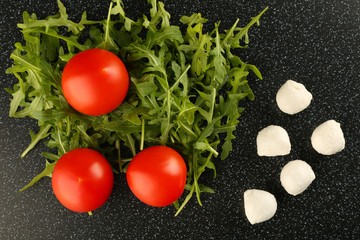 salad ingredients with mozzarella cheese, arugula and tomatoes on black background top view