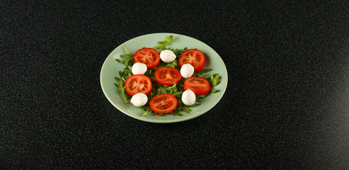 salad with mozzarella cheese, arugula and tomatoes on black background top view