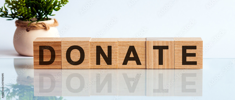 Poster donate message word on a wooden desk on cube blocks with a flower on background