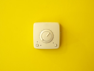 An electrical switch in the center on a yellow wall. Frontal view.