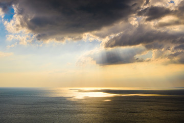 Large dark clouds over the sea. The sun's rays shine through the clouds and are reflected on the sea.