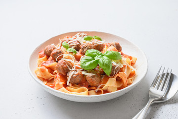 Pasta fettuccine with meatballs and tomatoes sauce in bowl on white table. Close up.