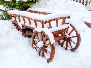 Fototapeta na wymiar Wooden red decorative cart stands in a snowdrift covered with snow
