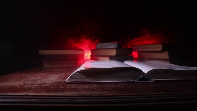 A stack of old books. Vintage book on wooden table. Magic lightning around a glowing book in the room of darkness. Selective focus