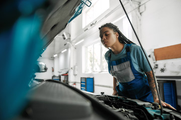 Autocare. Young african american woman, professional female mechanic opening car hood and checking car at auto repair shop