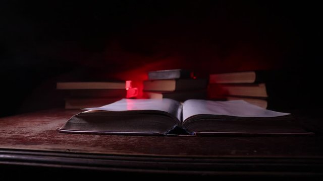 A stack of old books. Vintage book on wooden table. Magic lightning around a glowing book in the room of darkness. Selective focus