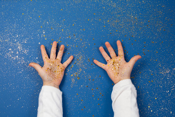 Child's hands holding golden stars on sparkling blue background.