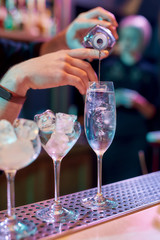 Close up of hands of male bartender pouring, mixing ingredients while making classic cocktail alcoholic drink at the bar counter in the night club