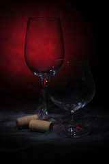 Empty glasses for wine and cognac, two corks of wine shrouded in smoke on a dark black and red background.