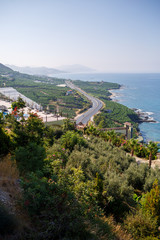 Fototapeta na wymiar An empty asphalt road winds along the breathtaking scenic coastline on a sunny summer day. A spectacular shot of a coastal road overlooking clear blue skies and the calm Mediterranean Sea.