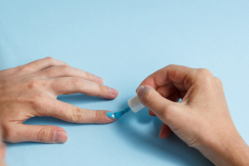 woman at a nail care procedure. a manicurist paints a girl's nails on her hand with blue nail polish