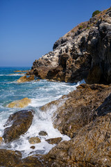 Fototapeta na wymiar Wonderful views of the blue Mediterranean Sea. Sunny rocks, waves with foam and splashing water. The wave crashes into the rocks on the shore