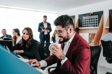 Mexican man with beard holding a coffee cup and working with computer at office in Mexico