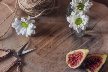 Purple fig fruit, daisy flowers  and a pair of coppery scissors on a wooden table, close up, still life photography