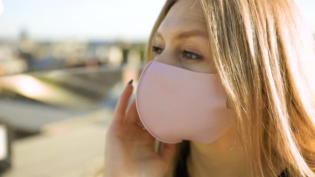 Close view of young blonde model with large eyes wearing medical face mask during quarantine on restaurant terrace