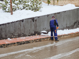 A janitor in blue uniforms removes snow with a shovel from the sidewalk on the street