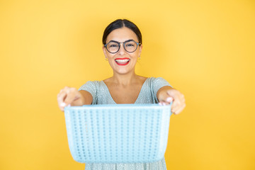 Young beautiful woman wearing glasses standing over isolated yellow background holding an empty...