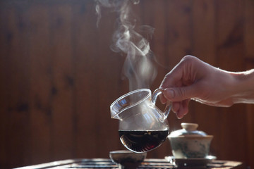 hand holds glass teapot with black chinese tea