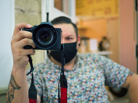 Fotógrafo hombre joven con tatuajes tomando una foto en una cafetería vistiendo mascarilla durante la nueva normalidad