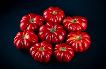 A group of Costoluto Fiorentino Tomatos (solanum lycopersicum). Big steak tomatoes on each other. Close up picture with dark background.