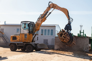 An industrial loader loads logs into a conveyor at a sawmill