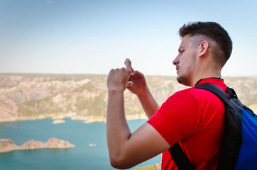 Joven tomando fotos de un paisaje de montaña. Joven sujetando un teléfono móvil.