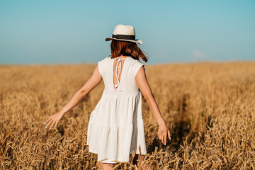 young girl happily walks in slow motion through a yellow field, touching the ears of wheat with her hands. Beautiful carefree woman enjoying nature and sunlight in a wheat field