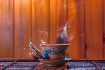 Traditional chinese painted clay tea brewing cup with cloud of steam and splashing hot water on wooden background