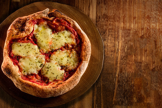 Brazilian pizza with mozzarella cheese, tomato sauce and oregano, on a round board. Traditional Brazilian Pizza. Top view on wood background and space for text.