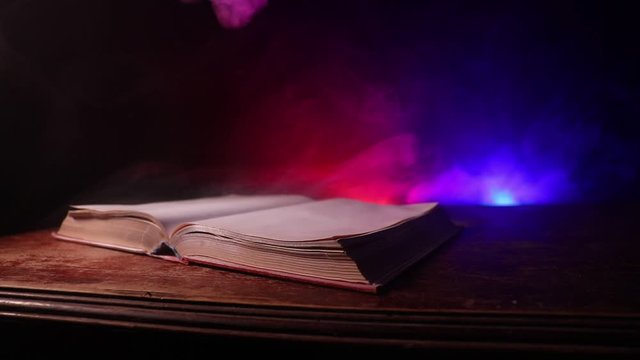 A stack of old books. Vintage book on wooden table. Magic lightning around a glowing book in the room of darkness. Selective focus