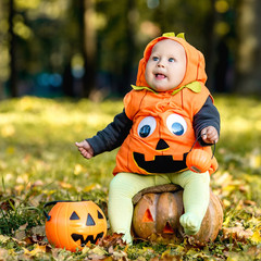 Child in pumpkin suit on background of autumn leaves
