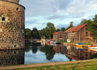 Fototapeta premium Houses Mirroring In The Moat Of Vadstena Castle At Dusk On A Sunny Summer Day With Some Clouds In The Sky