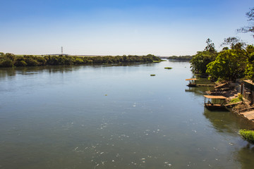 Scenic view of the Pardo River, wide and flowing, surrounded by lush forested banks under a bright sunny sky, located between Guaíra and Barretos in São Paulo, Brazil.