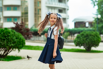 Fototapeta premium a beautiful girl, in a blue school uniform, with a school backpack, near the school building. Return to school, September 1