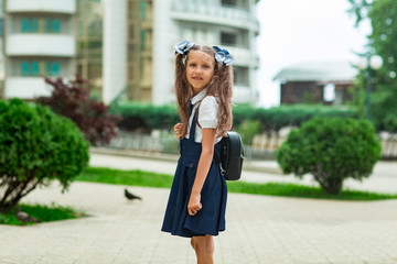 Fototapeta premium a beautiful girl, in a blue school uniform, with a school backpack, near the school building. Return to school, September 1