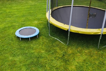 small trampoline on big round mat, size comparison, green lawn background