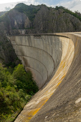 Panoramic photo of Vidraru dam or Barajul Vidraru in Romania, a concrete hydroelectric power plant dam built  in the carpathian mountains on a cloud dull summer day.