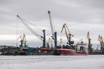 Red cargo ship at the winter stop in the industrial port frozen in the ice