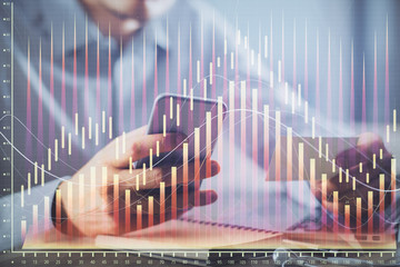 Double exposure of man's hands holding and using a phone and financial graph drawing. Analysis concept.