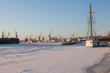 Fototapeta premium A white sailboat in the winter parking is frozen into the ice. Training ship. Saint Petersburg