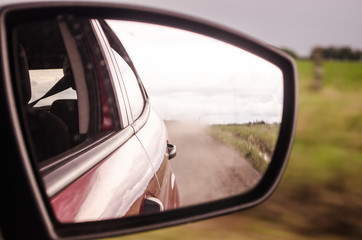 Fototapeta na wymiar Rearview mirror reflection of a car on a dusty road.