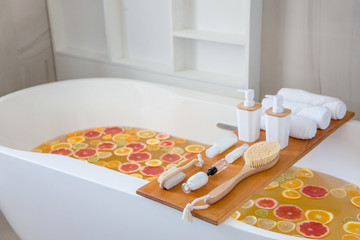Bathtub filling with water, mixed slices of fresh citrus fruits and spa set of natural product.