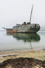 An old wooden Soviet whaling boat, the ship ran aground on the Bay shore, the front background is the sea shore, the background is the horizon with peninsulas, Vityaz Bay.