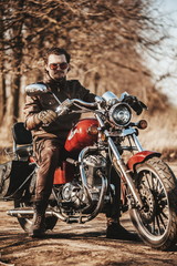 Fototapeta na wymiar Full leather suited biker on chopper looks grave in forest sunrise