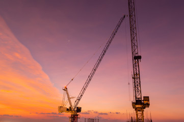 Huge crane and construction plant.Tower Crane in Construction site. Industrial construction cranes and building silhouettes over sun at sunrise.Construction crane and skyscraper at sunset