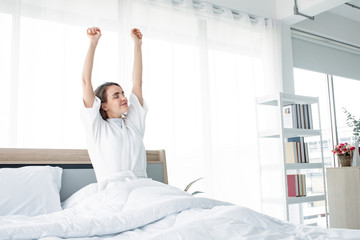 Bright Caucasian woman with stretching after waking up in the morning on the white bed.